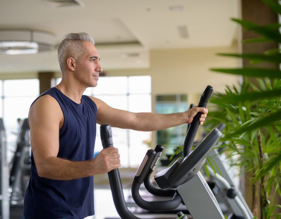 Mature Persian man exercising with elliptical trainer machine at the gym