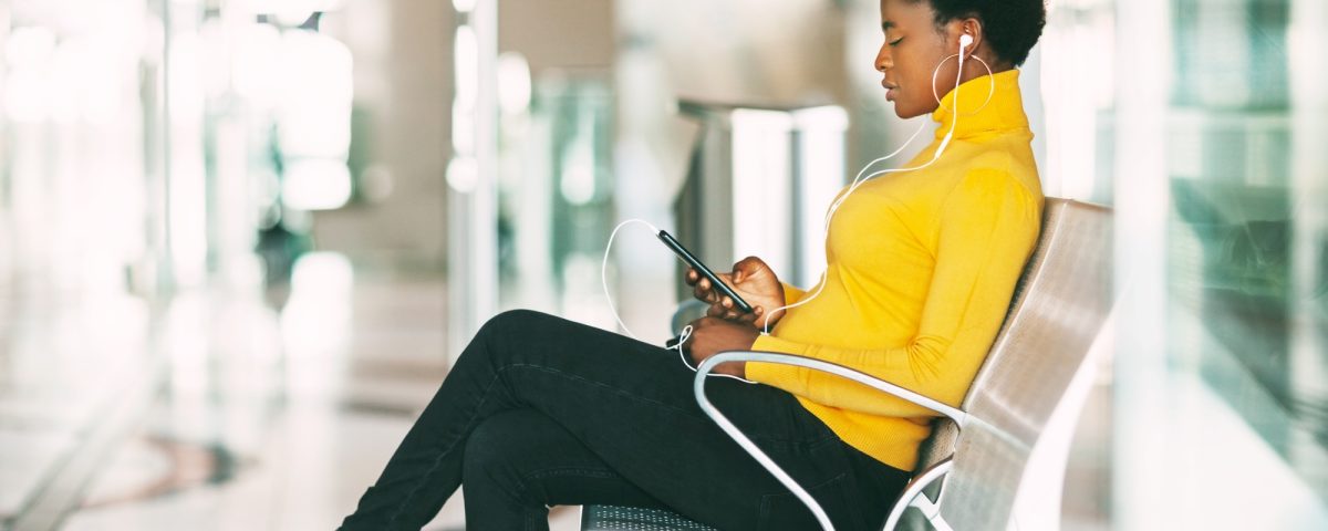Beautiful African woman sitting on a chair in the waiting room, waiting for a subway train and liste