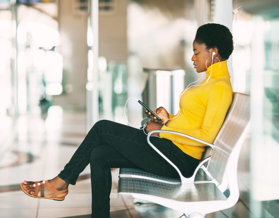 Beautiful African woman sitting on a chair in the waiting room, waiting for a subway train and liste