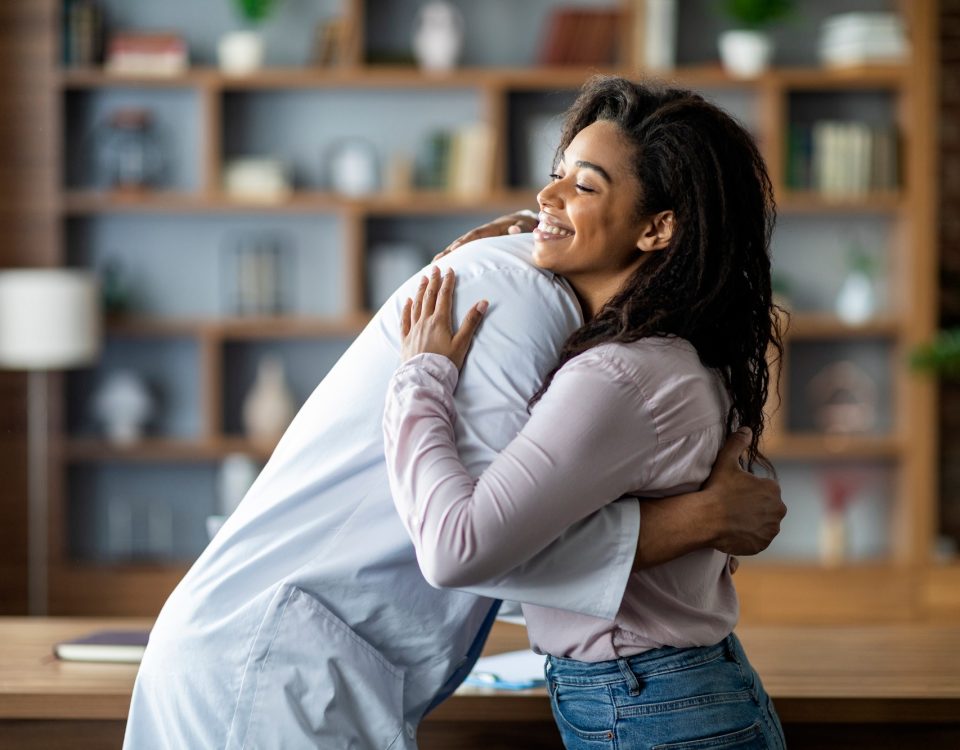 Doctor hugging cheerful black lady patient, clinic interior
