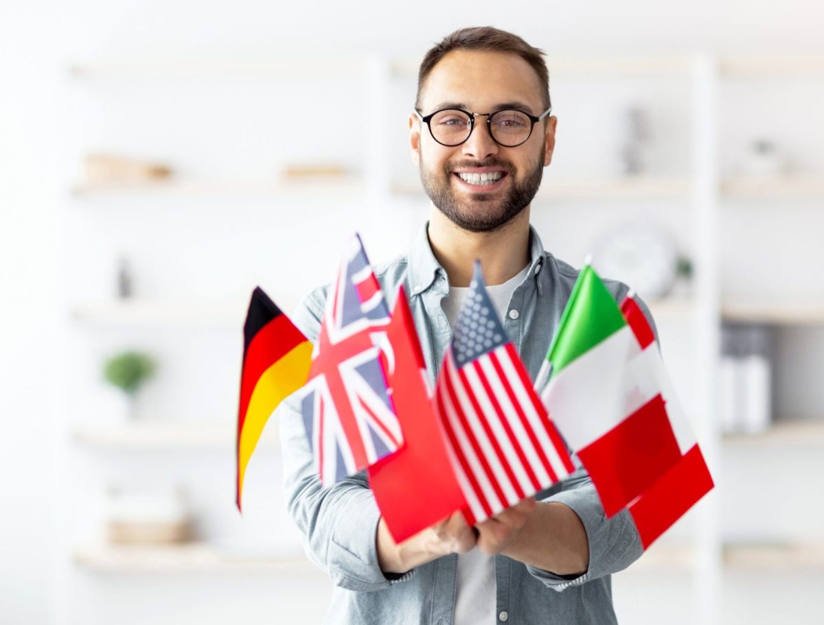 Modern education and student exchange. Cheerful young Caucasian guy holding a bunch of different flags at home.