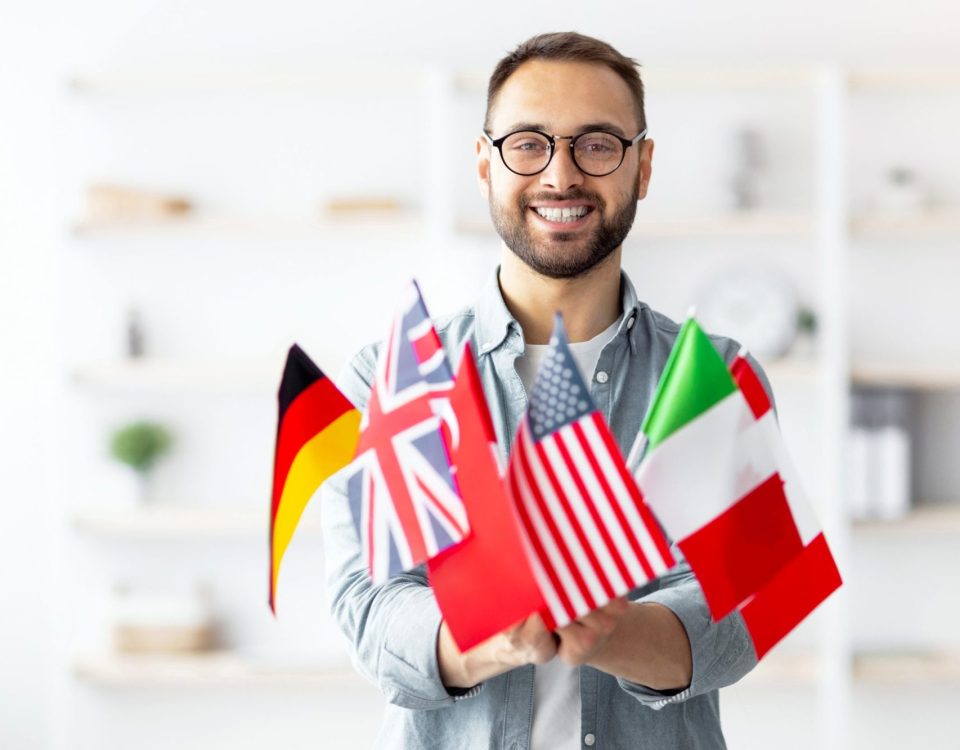 Des Technologies Non Disponibles au Canada 31 Modern education and student exchange. Cheerful young Caucasian guy holding a bunch of different flags at home.